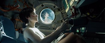 Movie still from “Gravity” (2013), directed by Alfonso Cuarón – A woman sitting in a space ship looking out a window; Medium shot, Overhead angle