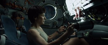 Movie still from “Gravity” (2013), directed by Alfonso Cuarón – A woman sitting inside of a space ship looking at her cell phone; Medium shot, Low angle