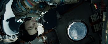 Movie still from “Gravity” (2013), directed by Alfonso Cuarón – A person in a spacesuit looking out of a window; Medium shot, Overhead angle