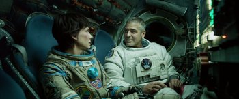 Movie still from “Gravity” (2013), directed by Alfonso Cuarón – Two people in spacesuits are sitting next to each other; Medium shot, Overhead angle