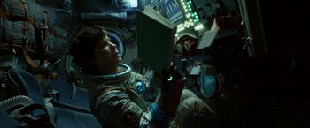 Movie still from “Gravity” (2013), directed by Alfonso Cuarón – A person in a spacesuit is reading a book; Medium shot, Overhead angle