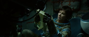 Movie still from “Gravity” (2013), directed by Alfonso Cuarón – A person in a space suit holding a book; Medium shot, Overhead angle