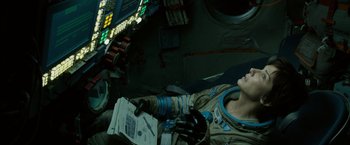 Movie still from “Gravity” (2013), directed by Alfonso Cuarón – A person in a space suit holding papers; Medium shot, Overhead angle