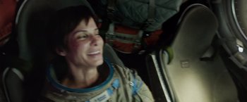 Movie still from “Gravity” (2013), directed by Alfonso Cuarón – A woman in a spacesuit smiling for the camera; Close Up shot, Overhead angle