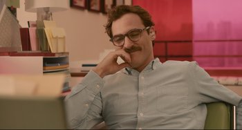 Movie still from “Her” (2013), directed by Spike Jonze – A man sitting in front of a red wall with his hand under his chin; Close Up shot, Over the shoulder angle