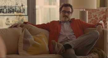 Movie still from “Her” (2013), directed by Spike Jonze – A man sitting on a couch wearing a red jacket; Medium shot, Over the shoulder angle