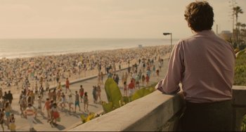 Movie still from “Her” (2013), directed by Spike Jonze – A man sitting on a ledge looking out at a crowded beach; Medium shot, Over the shoulder angle