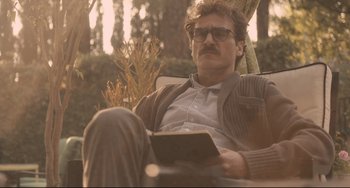 Movie still from “Her” (2013), directed by Spike Jonze – A man sitting in a chair reading a book; Medium shot, Low angle