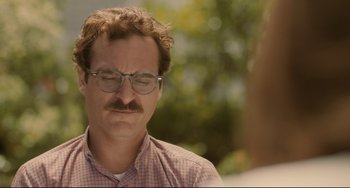 Movie still from “Her” (2013), directed by Spike Jonze – A man with a mustache and glasses is looking down; Close Up shot, Over the shoulder angle