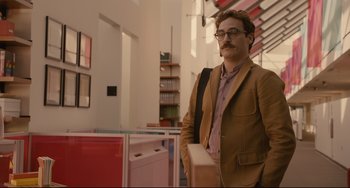 Movie still from “Her” (2013), directed by Spike Jonze – A man in a brown jacket holding a box in a room; Medium shot, Over the shoulder angle