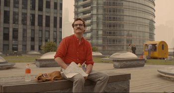 Movie still from “Her” (2013), directed by Spike Jonze – A man sitting on top of a bench in a city; Medium shot, Low angle