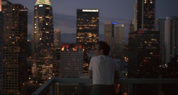Movie still from “Her” (2013), directed by Spike Jonze – A man standing on a balcony overlooking a city at night; Wide shot, High angle