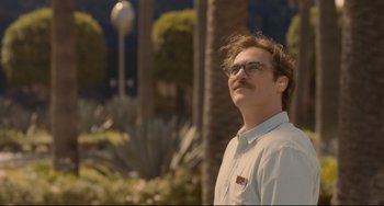 Movie still from “Her” (2013), directed by Spike Jonze – A man with a mustache wearing glasses standing in front of palm trees; Close Up shot, Over the shoulder angle