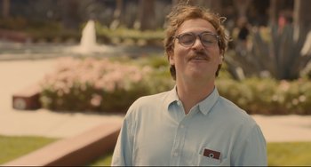 Movie still from “Her” (2013), directed by Spike Jonze – A man with a mustache wearing glasses standing in front of a fountain; Close Up shot, Over the shoulder angle