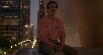 Movie still from “Her” (2013), directed by Spike Jonze – A man sitting on top of a ledge in front of a building; Medium shot, High angle