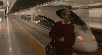 Movie still from “Her” (2013), directed by Spike Jonze – A man in a red jacket is standing in front of a train; Wide shot, High angle