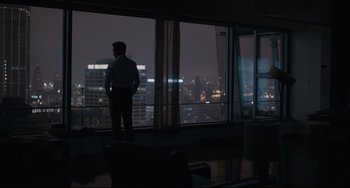 Movie still from “Her” (2013), directed by Spike Jonze – A man standing in front of a window looking out at a city; Wide shot, Over the shoulder angle