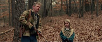 Movie still from “I, Tonya” (2017), directed by Craig Gillespie – A man standing next to a young girl holding a rifle; Medium shot, Over the shoulder angle