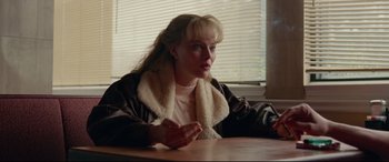 Movie still from “I, Tonya” (2017), directed by Craig Gillespie – A woman sitting at a wooden table in front of a window; Medium shot, Over the shoulder angle