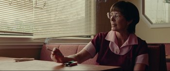 Movie still from “I, Tonya” (2017), directed by Craig Gillespie – An older woman sitting at a table with a cigarette in her hand; Close Up shot, Low angle