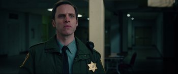 Movie still from “I, Tonya” (2017), directed by Craig Gillespie – A man in a sheriff's uniform stands in front of a building; Close Up shot, Over the shoulder angle