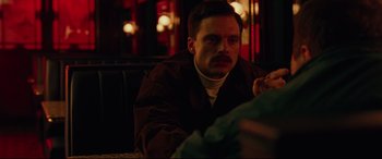 Movie still from “I, Tonya” (2017), directed by Craig Gillespie – A man sitting on a couch in front of a window; Close Up shot, Over the shoulder angle