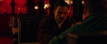 Movie still from “I, Tonya” (2017), directed by Craig Gillespie – A man sitting on a couch looking at something on his phone; Close Up shot, Over the shoulder angle