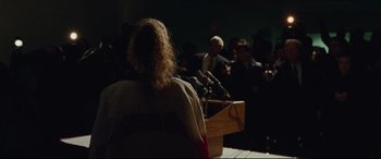 Movie still from “I, Tonya” (2017), directed by Craig Gillespie – A person standing in front of microphones at a press conference; Medium shot, Over the shoulder angle