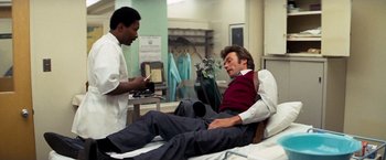 Movie still from “Dirty Harry” (1971), directed by Don Siegel – A man sitting on a hospital bed while a doctor looks at his cell phone; Medium shot, Low angle
