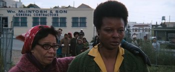 Movie still from “Dirty Harry” (1971), directed by Don Siegel – A woman in a green and yellow sweater standing in front of a crowd of onlookers; Close Up shot, Low angle