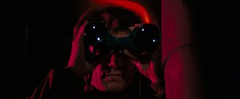 Movie still from “Dirty Harry” (1971), directed by Don Siegel – A man looking through binoculars in a dark room; Close Up shot, Low angle