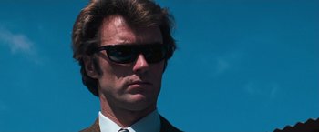 Movie still from “Dirty Harry” (1971), directed by Don Siegel – A person wearing a suit and sunglasses; Close Up shot, Low angle