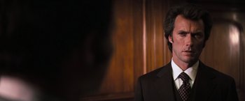 Movie still from “Dirty Harry” (1971), directed by Don Siegel – A man wearing a suit and tie in front of a wooden wall; Close Up shot, Over the shoulder angle