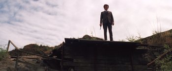 Movie still from “Dirty Harry” (1971), directed by Don Siegel – A man standing on top of a wooden structure holding a gun; Wide shot, Low angle