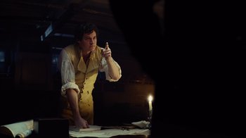 Movie still from “In the Heart of the Sea” (2015), directed by Ron Howard – A man holding a pen in his right hand while standing in front of papers; Medium shot, Over the shoulder angle