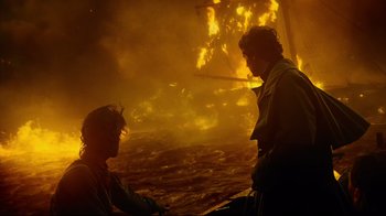 Movie still from “In the Heart of the Sea” (2015), directed by Ron Howard – Two men standing next to each other in front of a fire; Medium shot, Over the shoulder angle