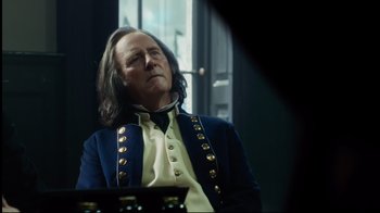 Movie still from “In the Heart of the Sea” (2015), directed by Ron Howard – A man with long black hair sitting in front of a window; Close Up shot, Over the shoulder angle