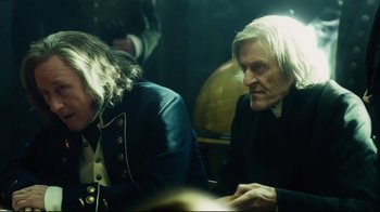 Movie still from “In the Heart of the Sea” (2015), directed by Ron Howard – Two men sitting at a table in a dark room; Medium shot, Over the shoulder angle
