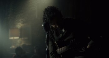 Movie still from “Inside Llewyn Davis” (2013), directed by Ethan Coen – A man playing a guitar in front of a microphone; Medium shot, Over the shoulder angle