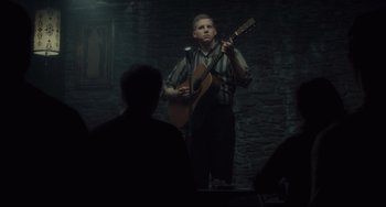 Movie still from “Inside Llewyn Davis” (2013), directed by Ethan Coen – A young man holding a guitar while standing in front of a group of people; Wide shot, Over the shoulder angle