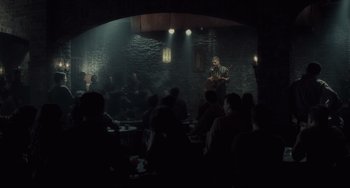 Movie still from “Inside Llewyn Davis” (2013), directed by Ethan Coen – A group of people sitting in a room with a man playing a guitar; Wide shot, Over the shoulder angle