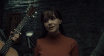 Movie still from “Inside Llewyn Davis” (2013), directed by Ethan Coen – A woman in a red sweater holding a microphone and a guitar; Close Up shot, Over the shoulder angle
