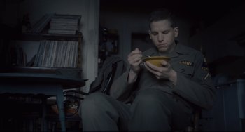 Movie still from “Inside Llewyn Davis” (2013), directed by Ethan Coen – A man sitting on a chair eating something; Medium shot, High angle