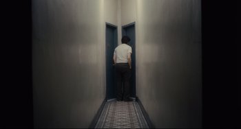Movie still from “Inside Llewyn Davis” (2013), directed by Ethan Coen – A man standing in a hallway with two doors open; Wide shot, High angle