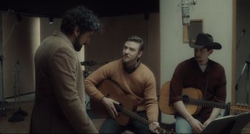 Movie still from “Inside Llewyn Davis” (2013), directed by Ethan Coen – A man is playing a guitar while another man watches; Medium shot, Over the shoulder angle