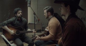 Movie still from “Inside Llewyn Davis” (2013), directed by Ethan Coen – A group of men sitting in a room with guitars; Medium shot, Over the shoulder angle