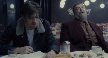 Movie still from “Inside Llewyn Davis” (2013), directed by Ethan Coen – Two people sitting at a table with food; Medium shot, Over the shoulder angle