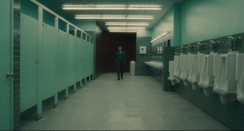 Movie still from “Inside Llewyn Davis” (2013), directed by Ethan Coen – A man standing in a bathroom next to urinals; Extreme Wide shot, High angle