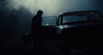 Movie still from “Inside Llewyn Davis” (2013), directed by Ethan Coen – A man standing in front of a car in the dark; Wide shot, Low angle