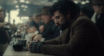 Movie still from “Inside Llewyn Davis” (2013), directed by Ethan Coen – A group of people sitting at a table with cups; Medium shot, Over the shoulder angle